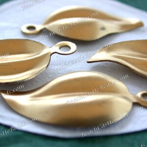 K&ouml;nnte beinhalten: Vier goldfarbene, metallene Anh&auml;nger in Blattform mit einem Loch oben zum Aufh&auml;ngen. Die Bl&auml;tter haben eine leicht strukturierte Oberfl&auml;che.