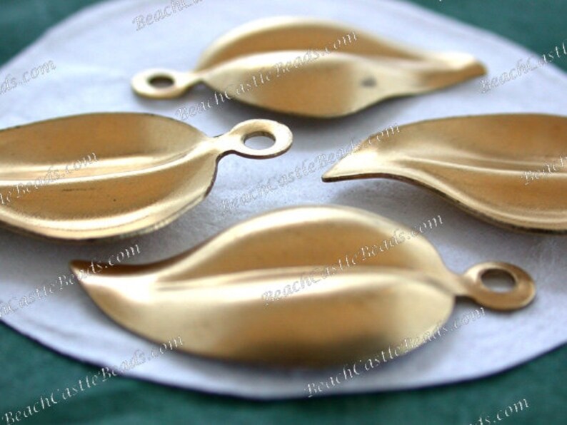 K&ouml;nnte beinhalten: Vier goldfarbene, metallene Anh&auml;nger in Blattform mit einem Loch oben zum Aufh&auml;ngen. Die Bl&auml;tter haben eine leicht strukturierte Oberfl&auml;che.