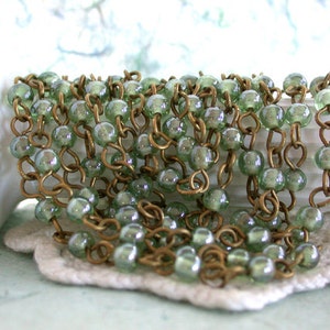 May include: A strand of green glass beads strung on a brass chain. The beads have a subtle iridescent sheen.