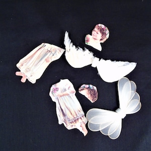 Puede incluir: Variedad de piezas de muñecas de papel vintage sobre un fondo negro. Las piezas incluyen un vestido, una cabeza con una corona floral, un par de alas y un vestido con un ramo. Los colores son pasteles suaves y blanco.