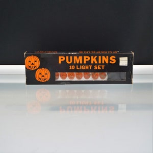 May include: A black rectangular cardboard box containing a 10 light set of small orange pumpkin-shaped bulbs. The box features the text PUMPKINS 10 LIGHT SET in orange lettering and includes illustrations of two jack-o'-lanterns on the left side.