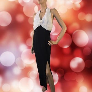 May include: A floor-length dress featuring a solid black skirt with a high side slit and a white halter-style bodice. The bodice includes a gathered fabric detail at the center of the neckline, creating a contrast between the white top and black skirt.