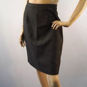 May include: A dark gray pencil skirt. The skirt is knee-length and has a tailored fit. The fabric appears to be a woven material. The skirt is displayed on a mannequin.