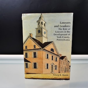 May include: A book titled "Lawyers and Leaders" with an illustration of a historic building with a clock tower. The book cover features the text "The Role of Lawyers in the Development of York County, Pennsylvania" and the author's name, Georg R. Sheets.