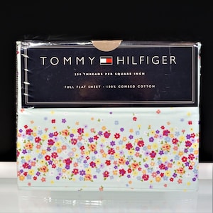 May include: A Tommy Hilfiger full flat sheet in light blue with a multicolored floral pattern. The packaging states 250 threads per square inch and 100% combed cotton. The sheet is wrapped in clear plastic with a dark blue label at the top.