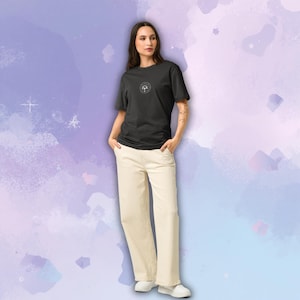 May include: A person wearing a black t-shirt with a circular graphic and cream-colored pants. The t-shirt has a small, white graphic on the chest. The pants are wide-legged and paired with white shoes. The background is a watercolor wash of purple and blue.