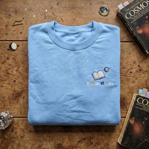Sweat à capuche brodé minimaliste Lost in Stories, sweat-shirt petite planète et livre, pull ras du cou livresque délicat, cadeau lecteur de l'espace, art littéraire