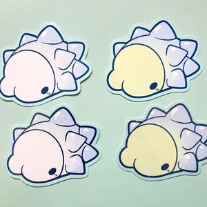 May include: Four die-cut stickers featuring a rounded, creature-like character with a spiky back. Two stickers have a pale pink face, and two have a pale yellow face. All have light blue spikes, dark blue outlines, and a small black eye.