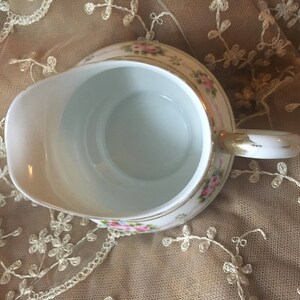 May include: A white porcelain creamer with a gold trim and floral design. The creamer has a handle and a spout.