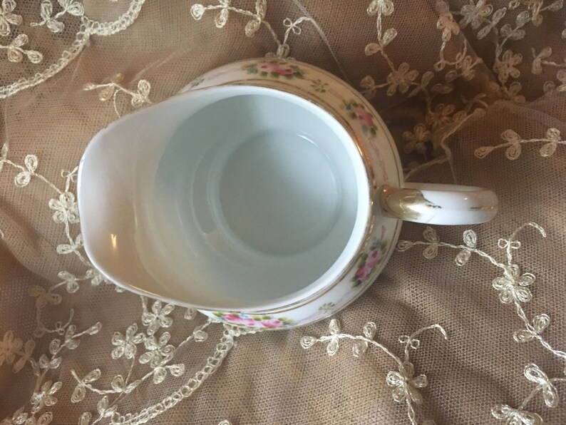 May include: A white porcelain creamer with a gold trim and floral design. The creamer has a handle and a spout.