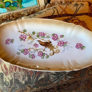 May include: White oval serving dish with a gold rim and a painted design of a brown bird with a long tail, perched on a branch with pink flowers.