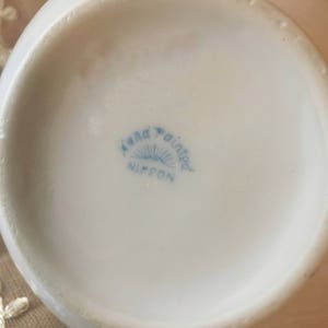 May include: Close-up of the bottom of a white ceramic bowl with a blue and white logo that reads "Hand Painted Nippon".