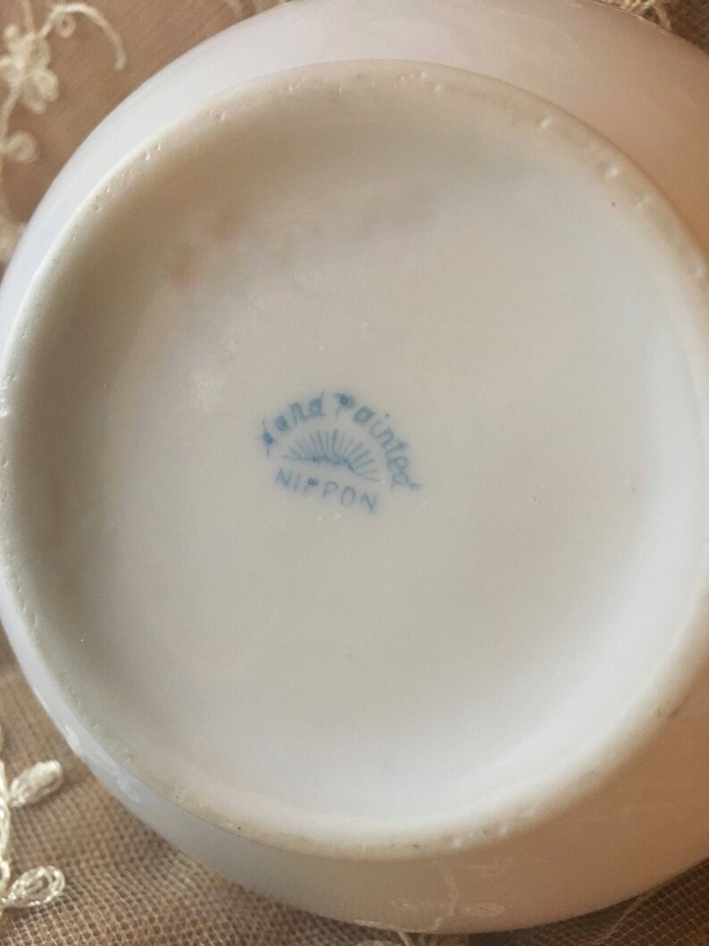 May include: Close-up of the bottom of a white ceramic bowl with a blue and white logo that reads "Hand Painted Nippon".
