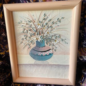 Puede incluir: Una pintura enmarcada de un jarrón azul y blanco con flores blancas. El jarrón tiene un patrón geométrico y las flores están pintadas en un estilo realista.