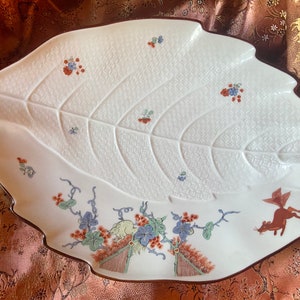 May include: A white ceramic serving dish shaped like a leaf with a brown rim. The dish is decorated with a stylised floral design and a small fox in the lower right corner.
