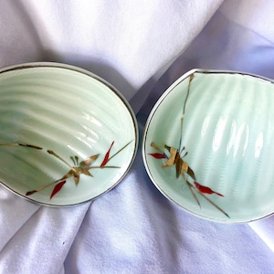 May include: Two light green ceramic bowls with a scalloped edge and gold trim. The bowls have a delicate floral design with red and gold accents.