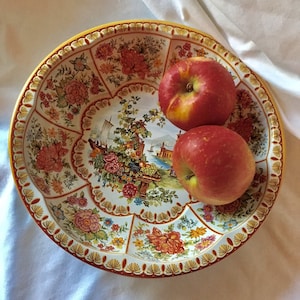May include: A vintage tin bowl with a floral design and a scalloped edge. Two red apples are in the bowl.