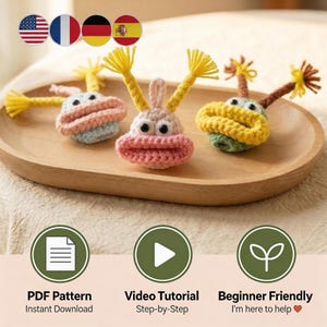 May include: Three handmade crochet creatures in pink, blue, and green with yellow and brown accents, arranged on a wooden tray. The creatures have large lips and eyes. The image also includes icons for a PDF pattern, video tutorial, and beginner-friendly instructions.
