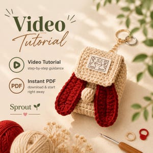 May include: A beige crochet pouch with a flap, featuring two long dark red ears and a small round tail. A metal keychain ring is attached to the top. A white fabric label with a rabbit illustration and the text HAND MADE is sewn on the flap.