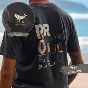 Op de afbeelding: Donkergrijs t-shirt met een walvisstaartafbeelding en het woord "PROTECT" in grote letters. De voorkant van het shirt heeft een klein wit walvislogo met de tekst "Protect what you love".