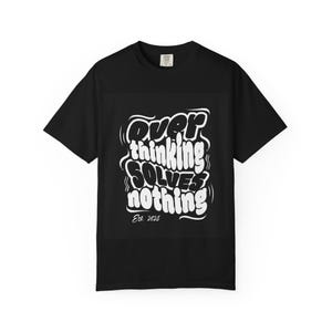 Puede incluir: Camiseta negra con texto blanco que dice "Overthinking Solves Nothing" en una fuente audaz y estilizada. El texto incluye "Est. 2025" debajo de la frase principal. La camiseta tiene mangas cortas y cuello redondo.