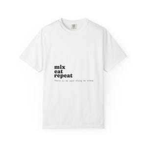 Op de afbeelding: Wit t-shirt met de woorden "mix eat repeat" verticaal gestapeld in zwart, met de zin "There is no such thing as sleep" eronder. Het shirt heeft een ronde hals en korte mouwen.