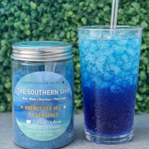 Op de afbeelding: Een pot blauwe energy-theemix en een glas blauwe drank met ijs. De pot heeft een label met de tekst "The Southern Ship Energy Tea Mix" met smaaknamen. De drank in het glas heeft een verloop van blauwtinten en een helder rietje.