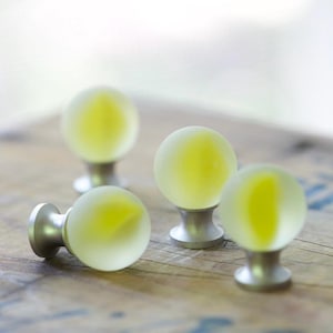 Può includere: Quattro pomelli per armadi con teste sferiche in vetro smerigliato e un nucleo giallo traslucido. Ogni pomello è montato su una base circolare in metallo argentato spazzolato, offrendo un design pulito per la ferramenta dei mobili.