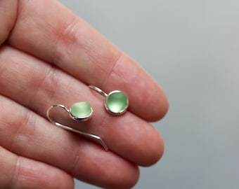 May include: A pair of silver earrings with light green glass stones. The earrings have a simple, minimalist design.