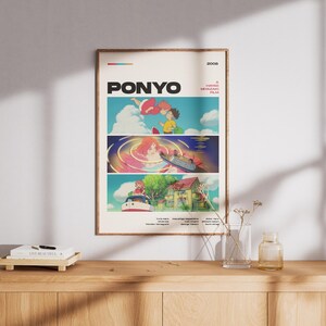 May include: A framed poster featuring the animated film "Ponyo." The poster has a beige background with three panels of colorful illustrations from the movie. The title "Ponyo" is in large, bold letters at the top.
