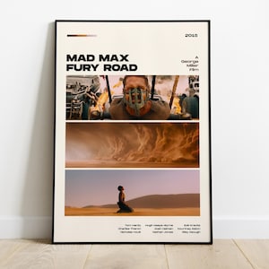 May include: A framed poster for the film "Mad Max: Fury Road" with a cream-colored background. The poster features three images from the movie, the title, the year 2015, and the director's name. The poster is displayed on a wooden floor.