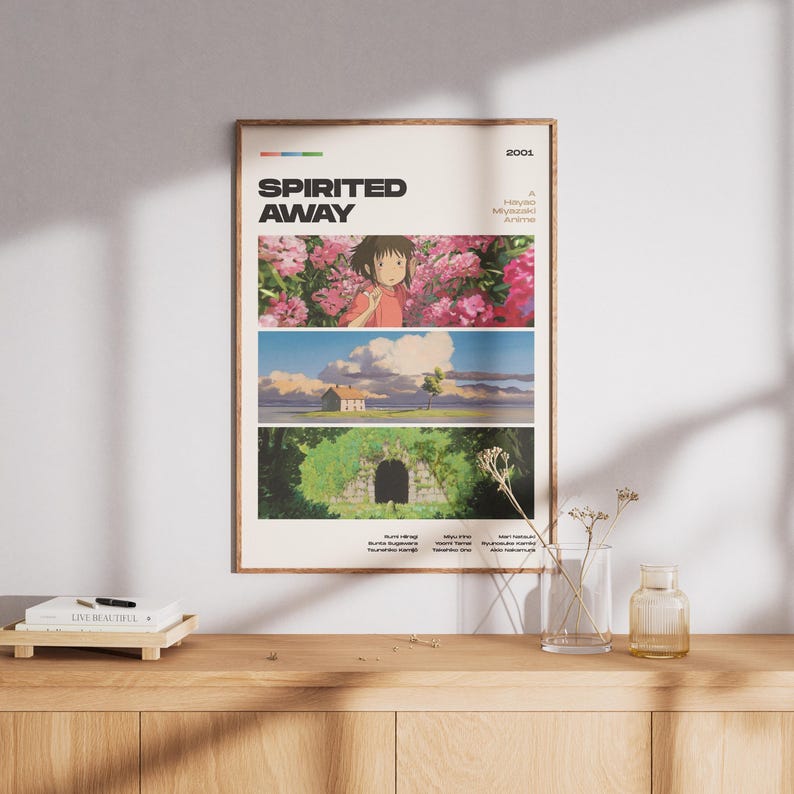 Op de afbeelding: Een ingelijste poster met de titel "Spirited Away" en drie panelen met kleurrijke beelden uit de animatiefilm. De poster heeft een beige achtergrond en een bruine lijst. Het jaar 2001 staat rechtsboven gedrukt.