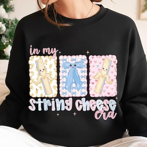 May include: Black sweatshirt with a playful design. The graphic shows three rectangular frames with cartoon images of a banana, a blue bow, and a banana. The text "in my String Cheese cra" is below the frames.