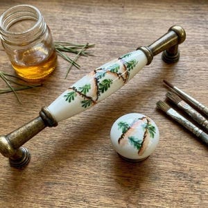 May include: A white ceramic mug with a black handle and the text "But First, Coffee" in a black, handwritten-style font. The mug is on a white surface.