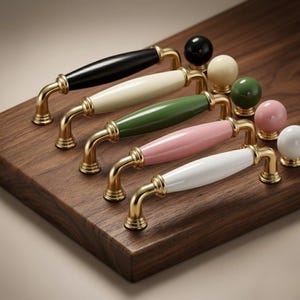 Pode incluir: Uma coleção de ferragens para armários, incluindo puxadores e puxadores. Os puxadores apresentam uma base dourada com um design curvo e centros de cerâmica coloridos: preto, creme, verde, rosa e branco. Os puxadores são redondos e combinam com os puxadores.