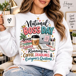 May include: A white crewneck sweatshirt featuring a colorful graphic print that reads National Boss Day Running on Coffee, Deadlines & Everyone's Questions, surrounded by illustrations of a coffee cup, books, a laptop, and office supplies.