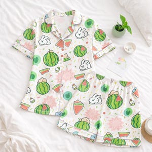 Puede incluir: Conjunto de pijama blanco con estampado de sand&iacute;a y conejito. La parte superior de manga corta tiene una parte delantera abotonada y un cuello con muescas. Los pantalones cortos tienen una cintura el&aacute;stica. El estampado incluye sand&iacute;as verdes, rodajas de sand&iacute;a rosas y conejitos blancos.