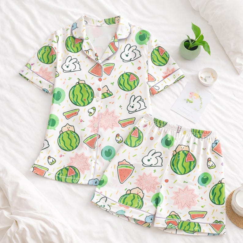 Puede incluir: Conjunto de pijama blanco con estampado de sand&iacute;a y conejito. La parte superior de manga corta tiene una parte delantera abotonada y un cuello con muescas. Los pantalones cortos tienen una cintura el&aacute;stica. El estampado incluye sand&iacute;as verdes, rodajas de sand&iacute;a rosas y conejitos blancos.