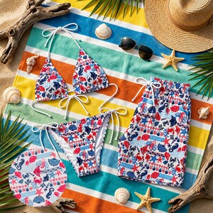 May include: A white bikini and matching swim trunks with a red, blue, and white nautical pattern are displayed on a striped beach towel. A straw hat, sunglasses, seashells, and starfish complete the beach scene.
