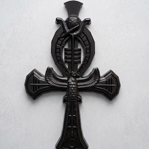 May include: A black ankh wall decoration featuring a central falcon with outstretched wings, an eye of Horus symbol at the top, and intricate geometric carvings throughout the cross structure, finished with a smooth, matte black surface texture.