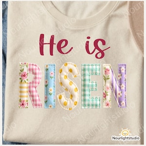 Könnte beinhalten: Cremefarbenes T-Shirt mit dem Schriftzug "He is Risen" in burgunderfarbener Schrift und Patchwork-Buchstaben. Die Buchstaben sind mit floralen, Vichy- und Polka-Dot-Mustern in Rosa, Blau, Gelb und Grün verziert.
