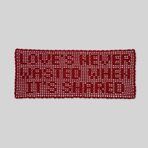 Puede incluir: Una pieza rectangular de ganchillo rojo con el texto LOVE IS NEVER WASTED WHEN IT IS SHARED. El diseño está creado con un patrón de rejilla calado, con las letras formadas por puntadas de hilo rojo sólido sobre el fondo abierto.