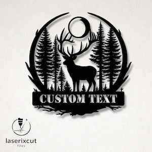 以下が含まれることがあります： 黒い金属製の壁の芸術。森のシーンにいる鹿のシルエット、松の木、月が描かれています。「CUSTOM TEXT」の文字が長方形のバナーに表示されています。デザインは円形のフレームで囲まれています。