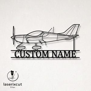 May include: A black metal wall art piece featuring a side profile outline of a single-engine propeller airplane. Below the aircraft, the text CUSTOM NAME is integrated into the design between two horizontal lines. The piece has a clean, laser-cut finish.