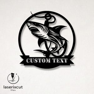 May include: Black metal wall art featuring a shark leaping out of the water, intertwined with an anchor. The design is set within a circular frame, with a banner below that reads "CUSTOM TEXT". The Laserixcut files logo is in the lower left corner.