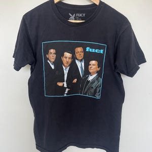 May include: Black t-shirt featuring a group of men in suits within a light blue rectangle. The word "fuct" is in light blue text. The shirt has a crew neck and the brand logo is visible.