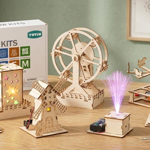 May include: A STEM kit set featuring wooden model components including a light-up star lantern, a windmill, a ferris wheel, a rotating carousel, and a fiber optic light. The set includes a white box labeled STEM KITS, flat wooden sheets, and a screwdriver.