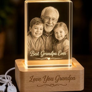 May include: A rectangular glass block featuring a laser-etched image of a grandfather with a young boy and girl, with the text Best Grandpa Ever. The block sits on a light wood base engraved with Love You Grandpa and a USB power cord.