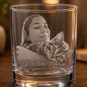 May include: A clear glass tumbler featuring a laser-etched portrait of a person holding a tabby cat. The engraving includes the text "Life Is Better With Cats" positioned below the image, accompanied by a small heart symbol centered underneath.
