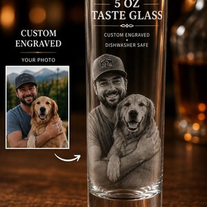 May include: A clear 5 oz taste glass featuring a custom engraving of a person wearing a baseball cap and hugging a golden retriever. The glass includes the text 5 OZ TASTE GLASS, CUSTOM ENGRAVED, and DISHWASHER SAFE, with a reference photo shown.